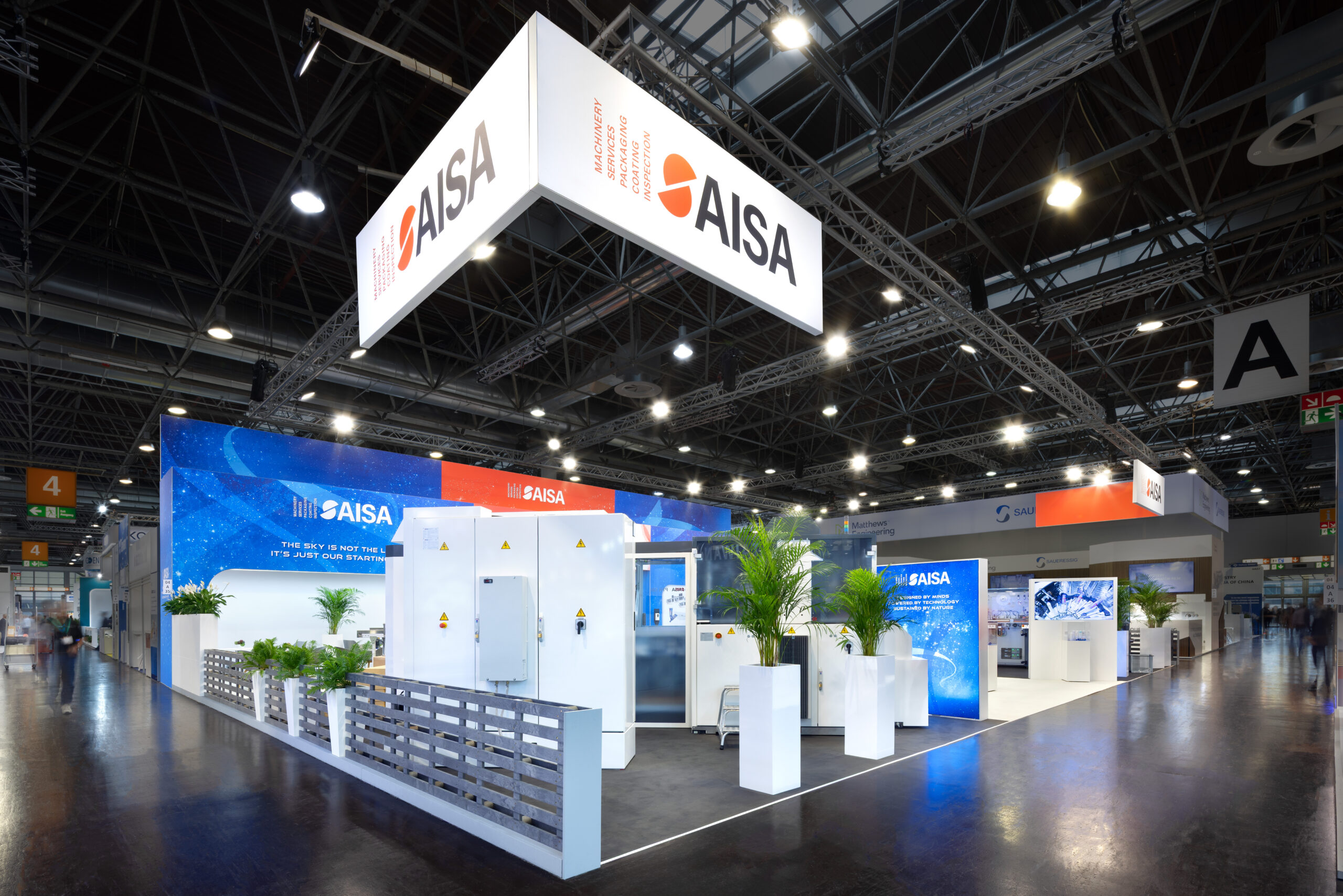 A large AISA exhibition booth featuring white machinery equipment, potted plants, a small fence border, and a prominent hanging overhead corporate sign
